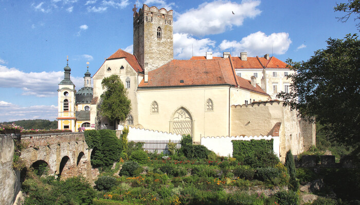 Gebäude vor der Burg mit Blumengarten unterhalb der Brücke