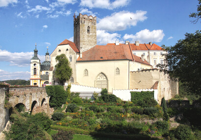 Gebäude vor der Burg mit Blumengarten unterhalb der Brücke